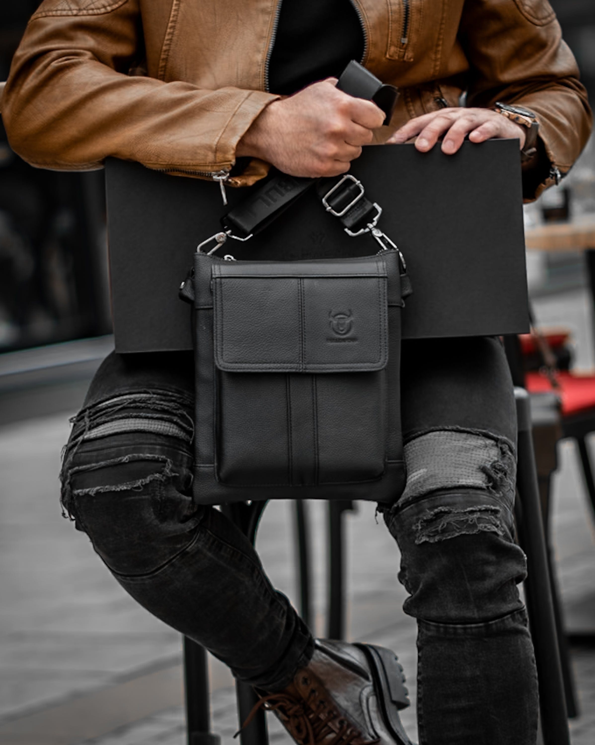 Muška kožna torba Toro - Crna Boja - Muškarac drži u rukama kaiš torbe i pokazuje prednju stranu