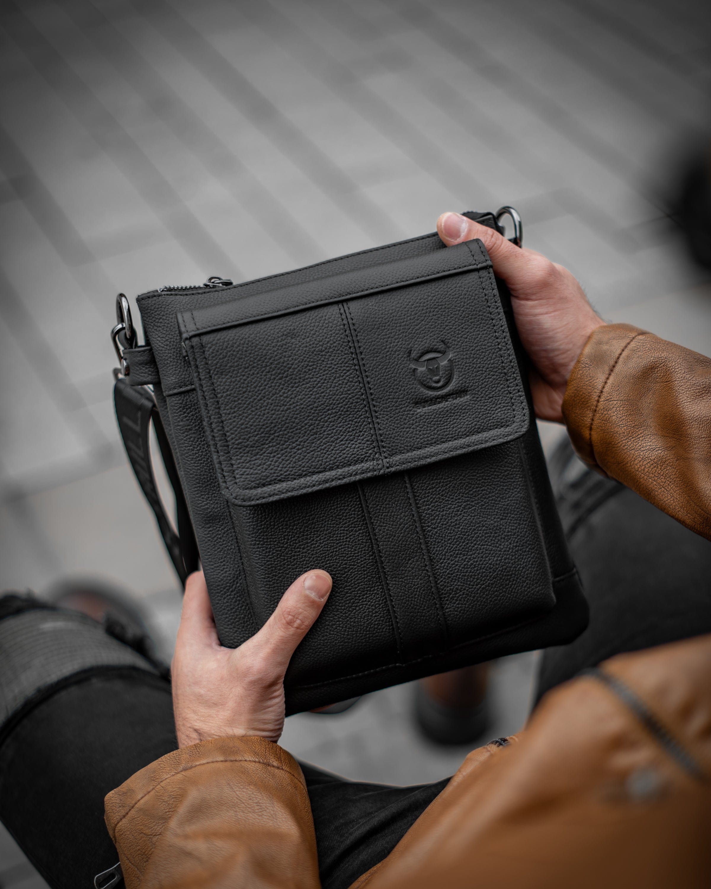 Muška kožna torba Toro - Crna Boja - Muškarac drži u rukama torbu i pokazuje prednju stranu i logo