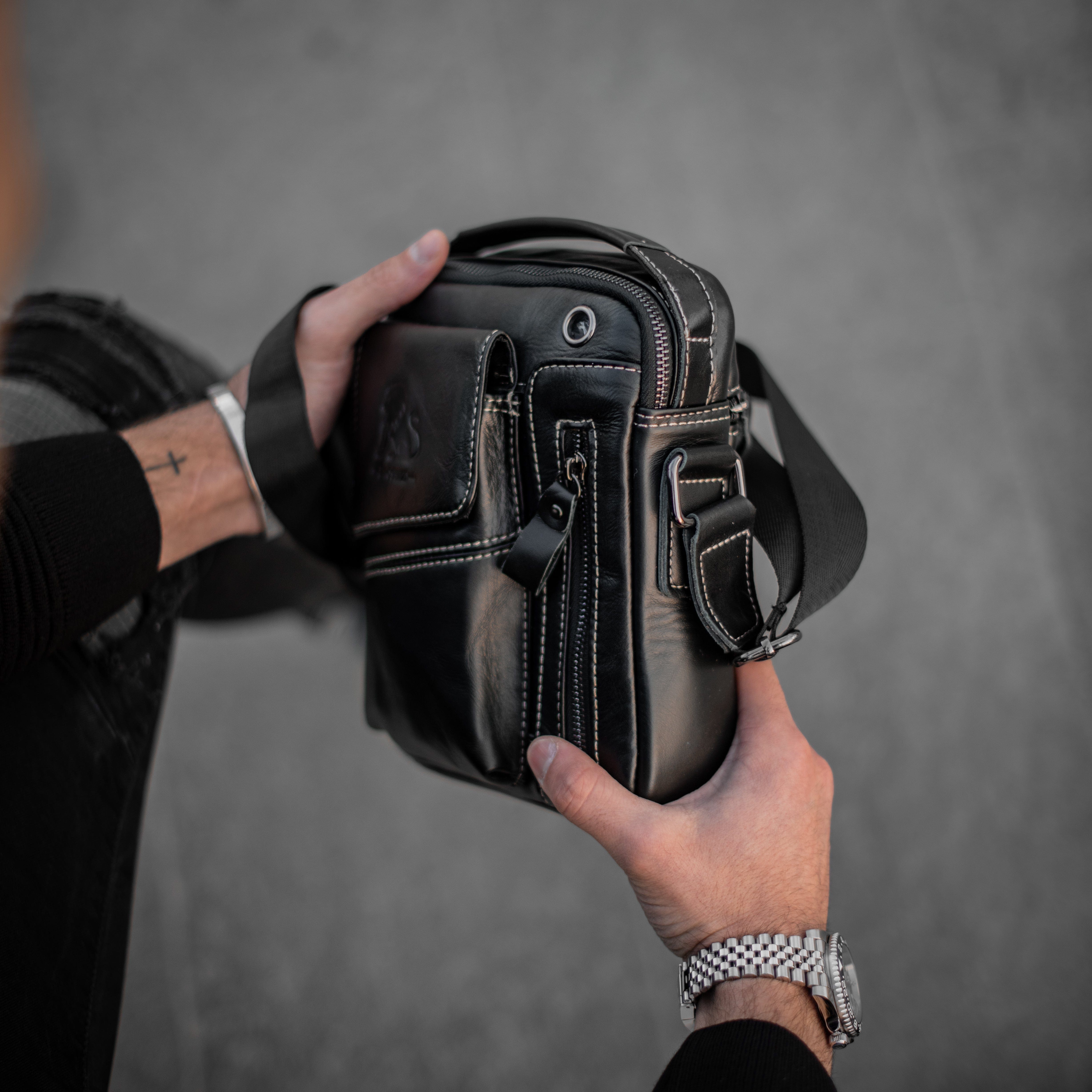 Muška Kožna Torba Leo - Crna Boja - Muskarac drzi u rukama i izbliza pokazuje prednju bočnu stranu torbe