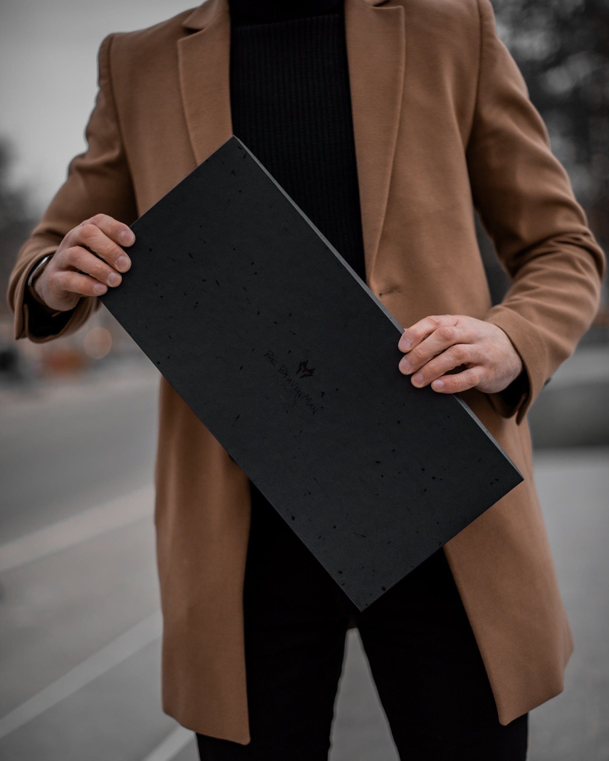 Muskarac pokazuje elegantnu kutiju u kojoj se dobija muska kozna torba Tour u svetlo braon boji.