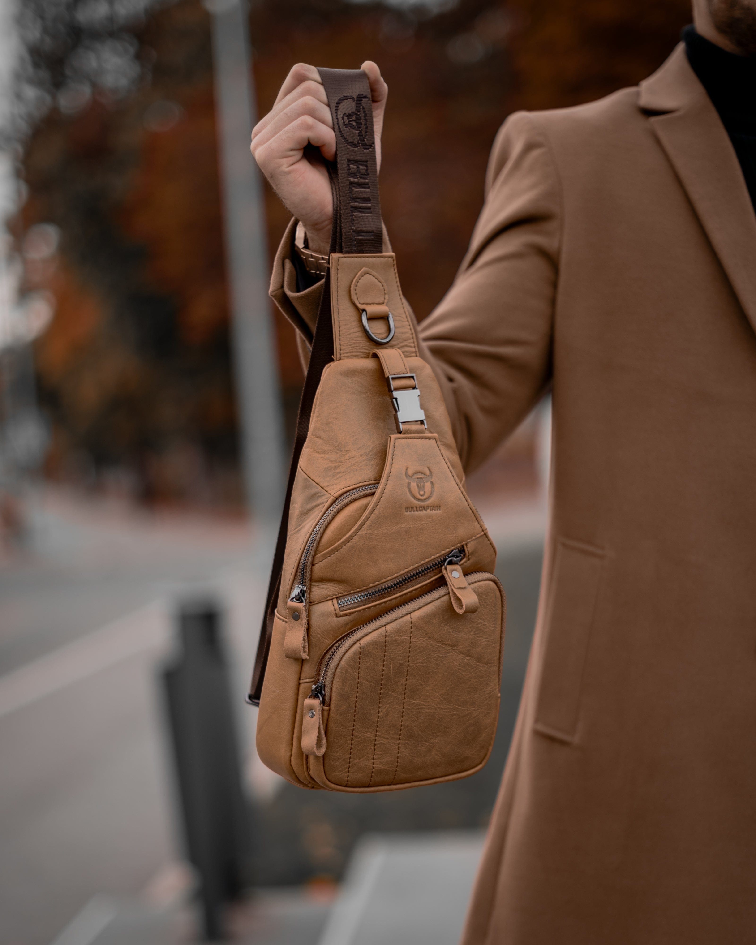 Muška Kožna Torba Tour - Svetla Braon Boja - Muskarac drzi u ruci kaiš i pokazuje torbu