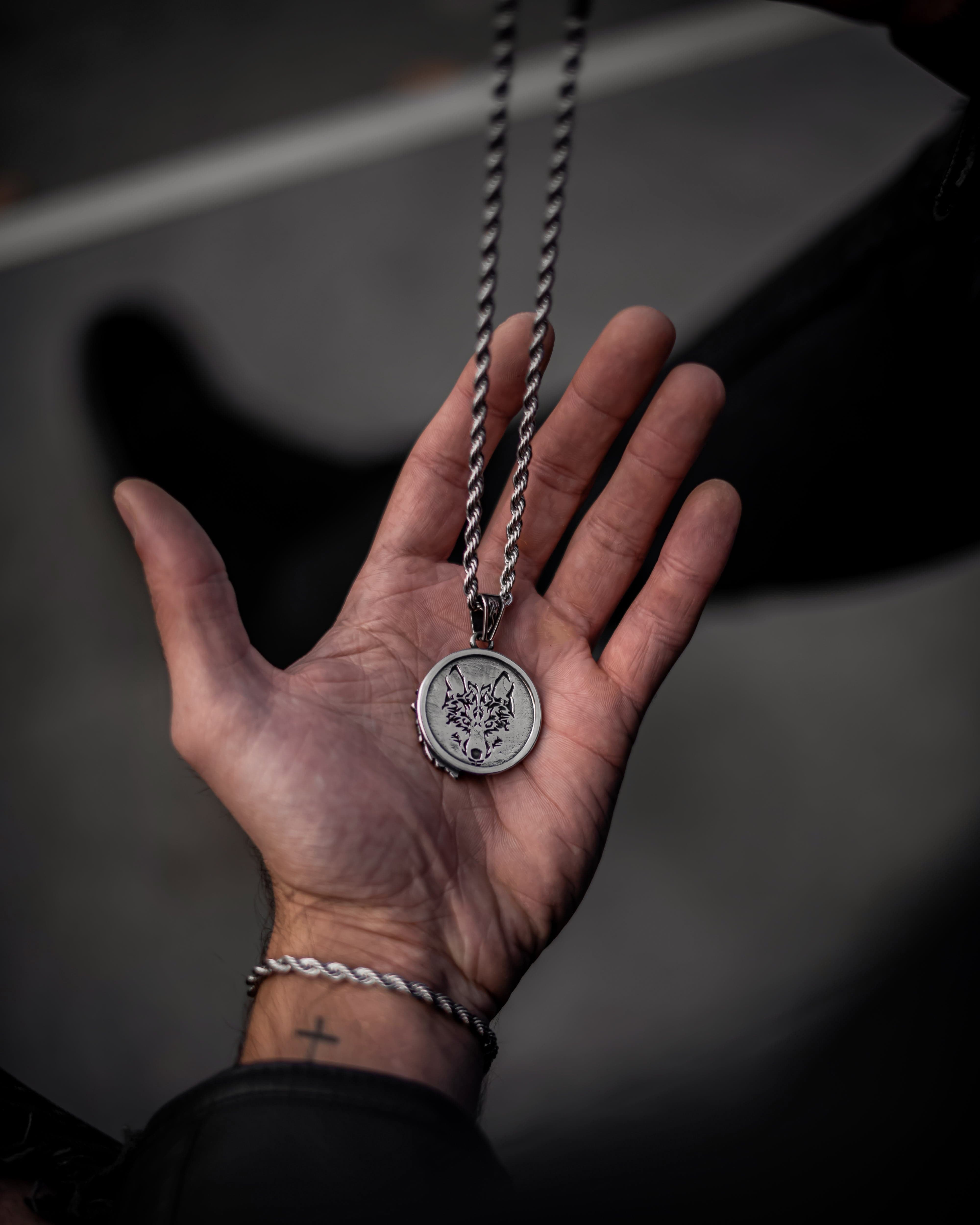 Muskarac drzi na dlanu i pokazuje zadnju stranu priveska muske ogrlice Lone Wolf, Privezak i lanac HIRUSKI CELIK, srebrna boja, Najbolja cena i prodaja u Srbiji, model 10