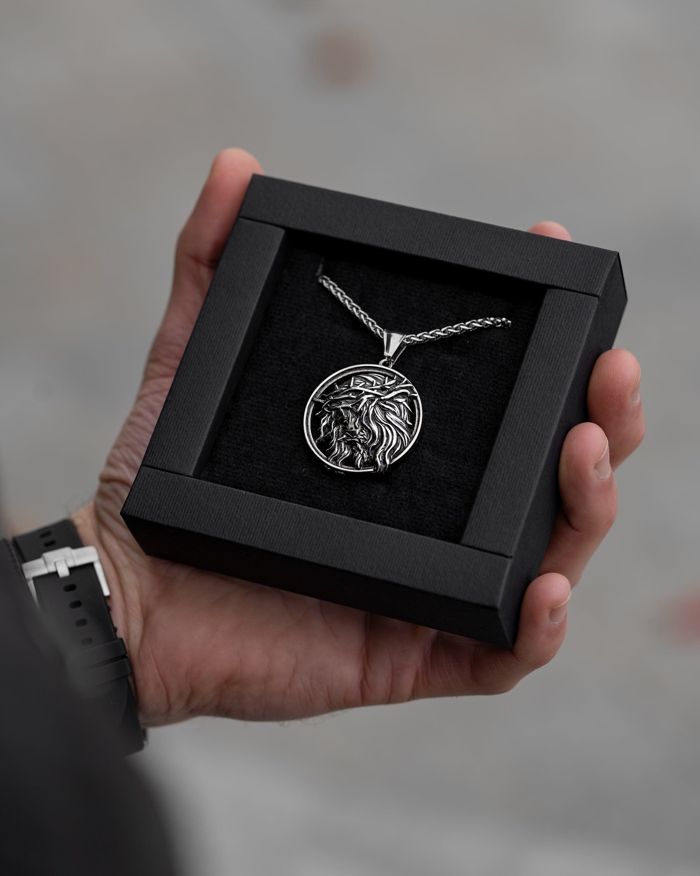 Muskarac drzi u ruci kutiju sa muskom ogrlicom Crown of Thorns, Privezak i lanac HIRUSKI CELIK, srebrna boja, Najbolja cena i prodaja u Srbiji, model 15