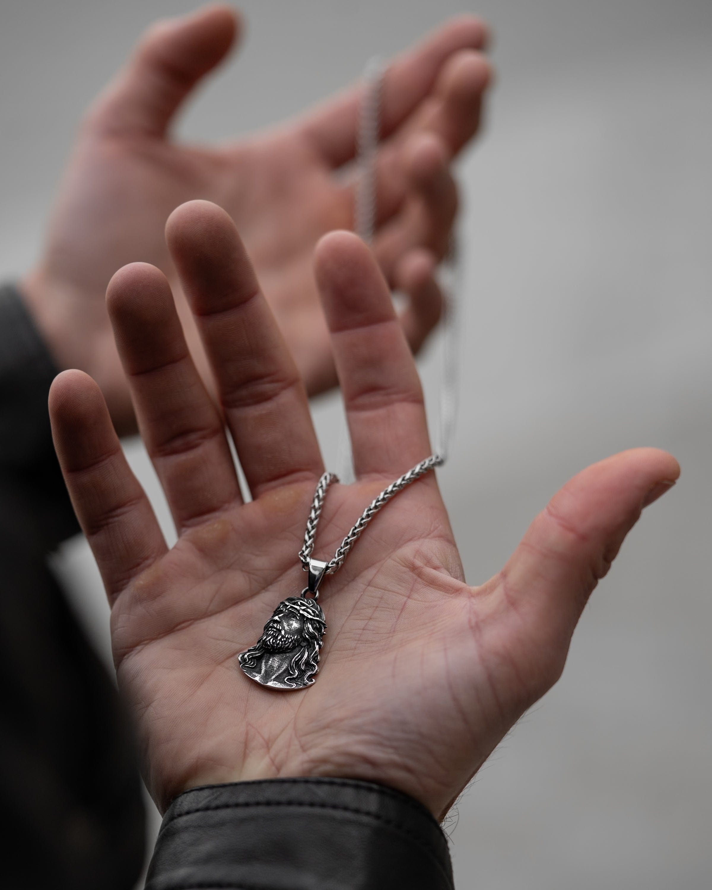 Muskarac drzi na dlanu i pokazuje prednju stranu priveska muske ogrlice Son of God, Privezak i lanac HIRUSKI CELIK, srebrna boja, Najbolja cena i prodaja u Srbiji, model 16