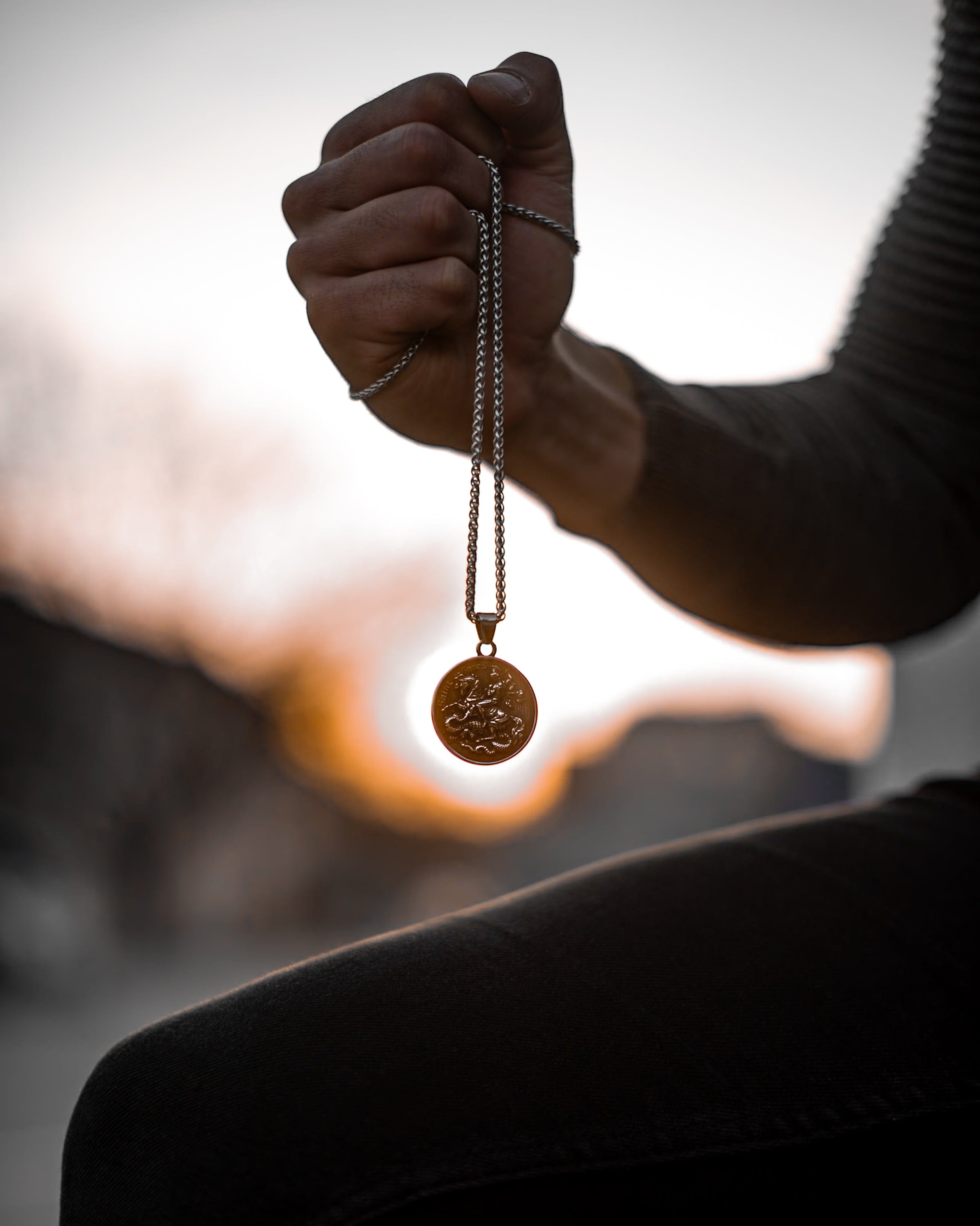Muskarac drzi u ruci musku ogrlicu Saint George, Privezak i lanac HIRUSKI CELIK, srebrna boja, Najbolja cena i prodaja u Srbiji, model 20