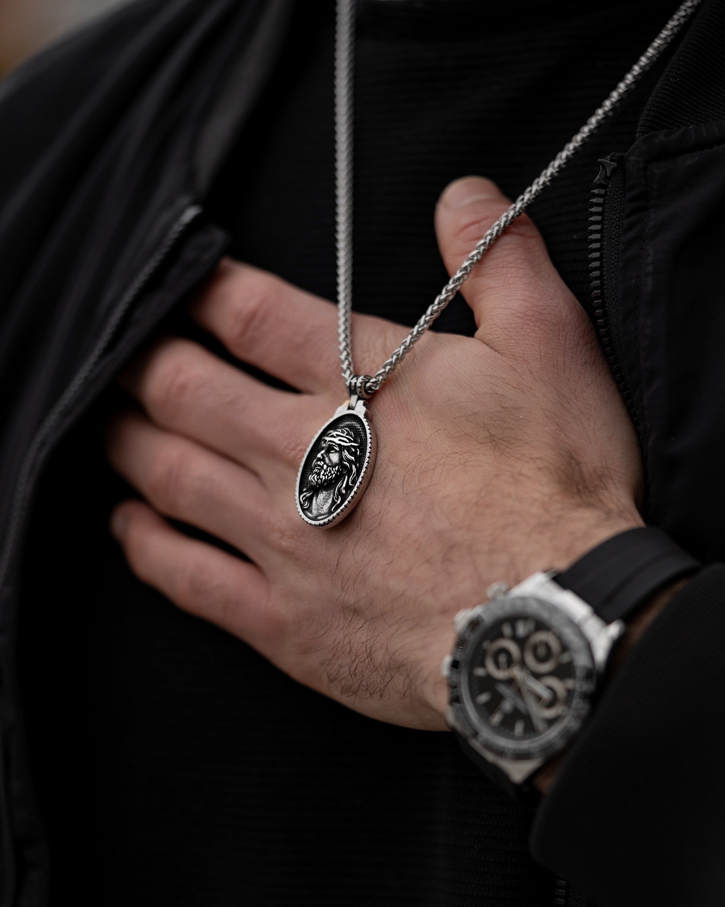 Muskarac nosi oko vrata i rukom prikazuje prednju stranu priveska muske ogrlice Jesus of Nazareth, Privezak i lanac HIRUSKI CELIK, srebrna boja, Najbolja cena i prodaja u Srbiji, model 21