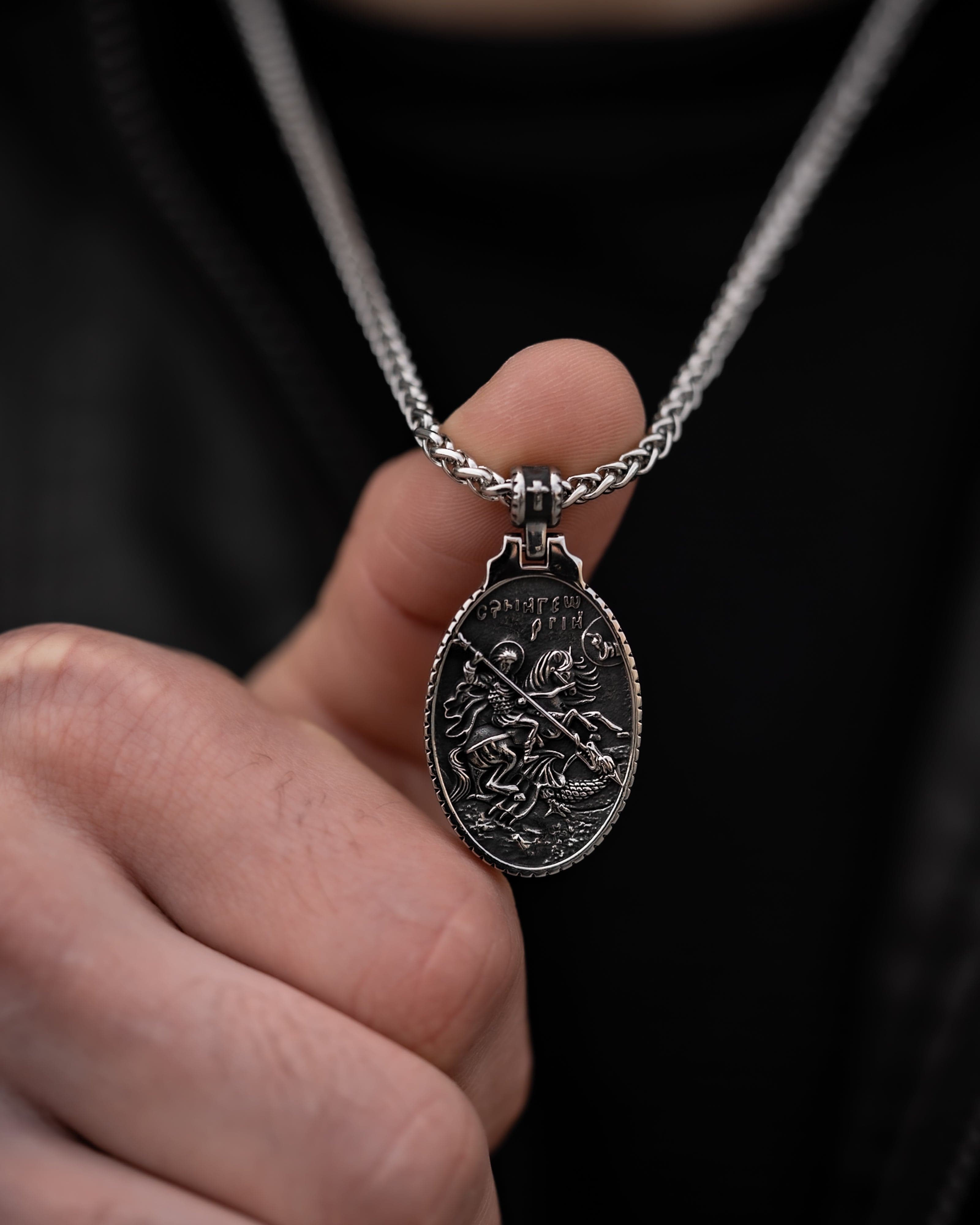 Muskarac detaljno pokazuje gravuru priveska muske ogrlice SV. Georgije Silver, Privezak i lanac HIRUSKI CELIK, srebrna boja, Najbolja cena i prodaja u Srbiji, model 25