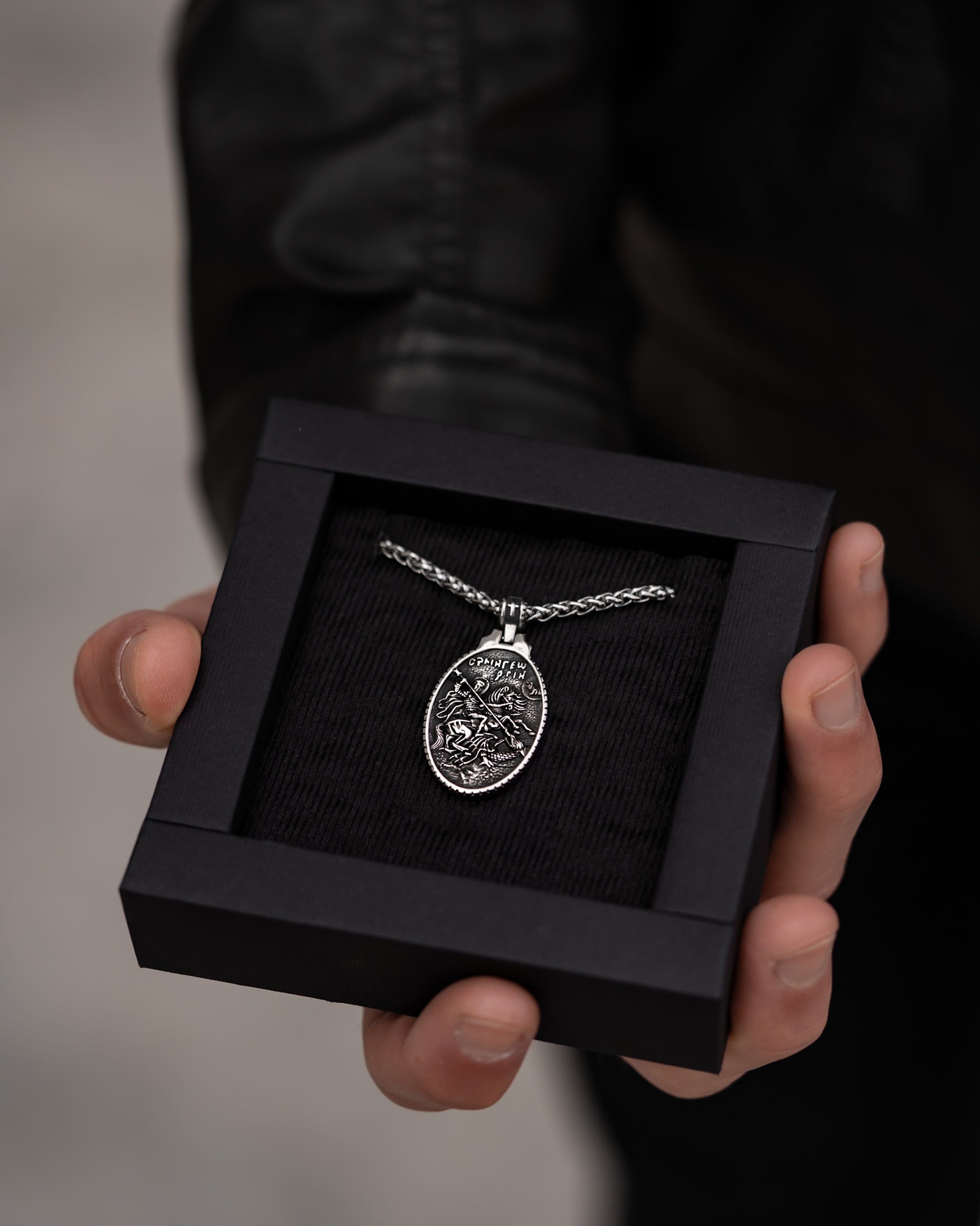 Muskarac drzi u ruci kutiju sa muskom ogrlicom SV. Georgije Silver, Privezak i lanac HIRUSKI CELIK, srebrna boja, model 25