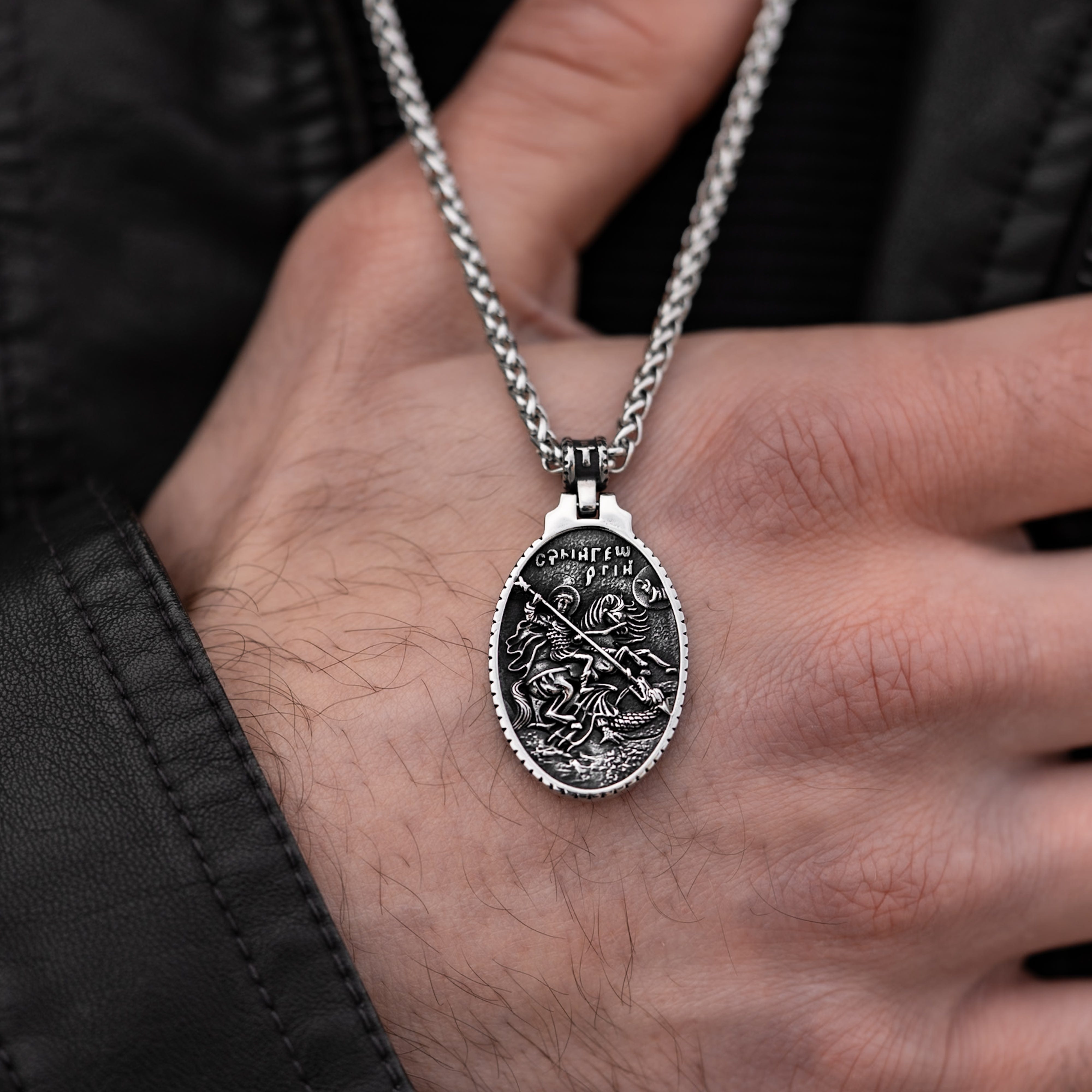 Muskarac rukom prikazuje detaljno privezak muske ogrlice SV. Georgije Silver, Privezak i lanac HIRUSKI CELIK, srebrna boja.