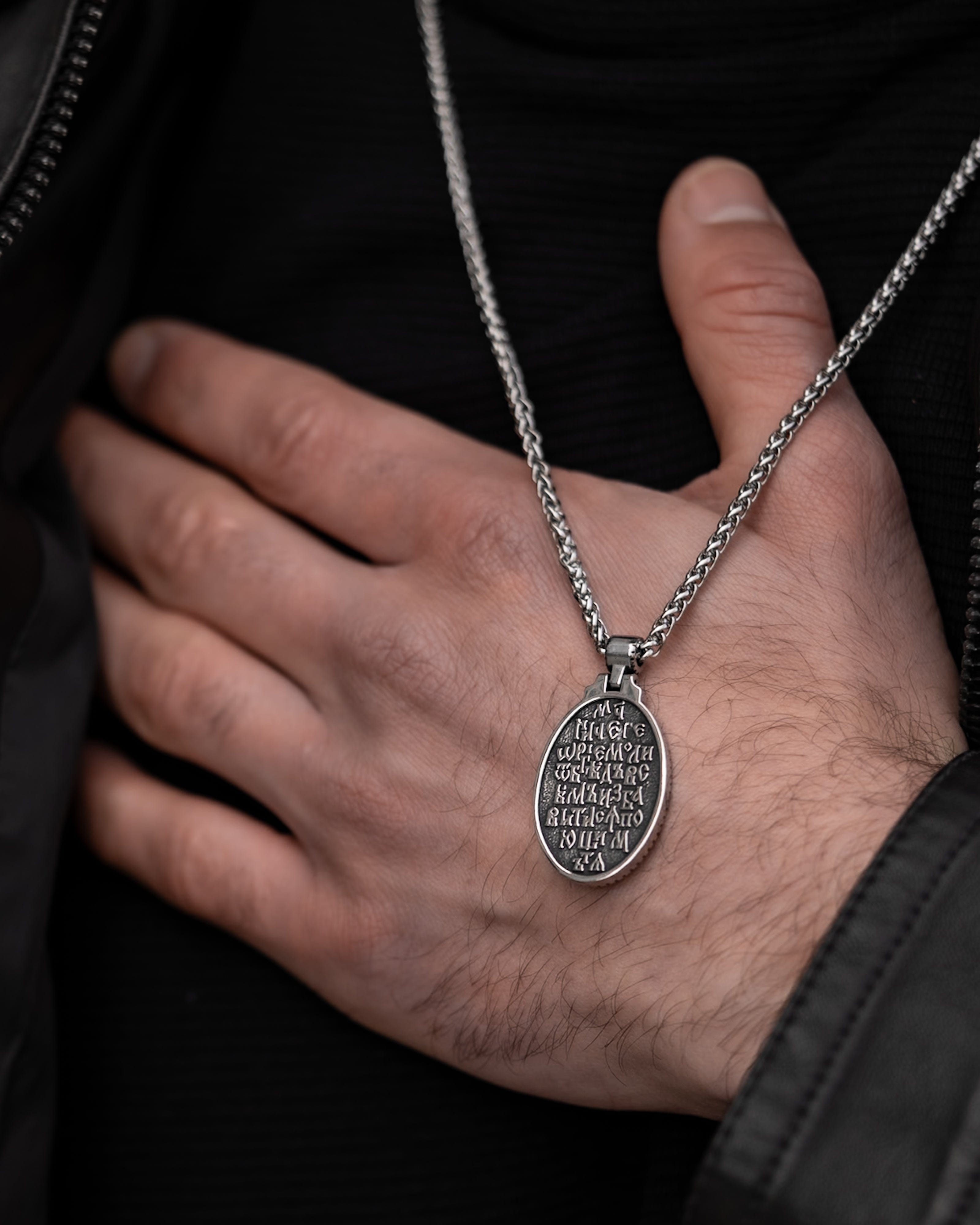 Muskarac rukom prikazuje zadnju stranu priveska muske ogrlice SV. Georgije Silver, Privezak i lanac HIRUSKI CELIK, srebrna boja, Najbolja cena i prodaja u Srbiji, model 25