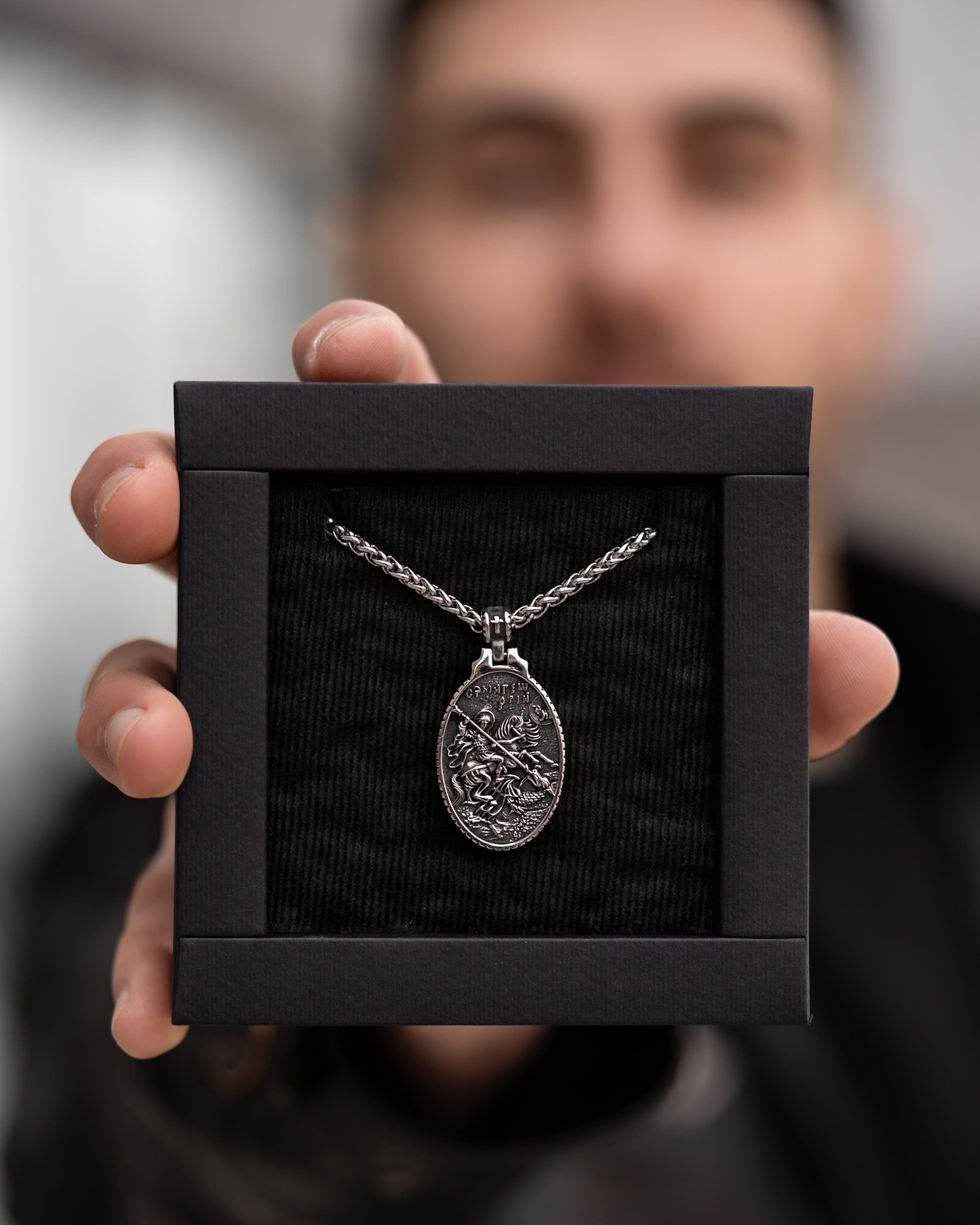 Muskarac pokazuje kutiju sa muskom ogrlicom SV. Georgije Silver, Privezak i lanac HIRUSKI CELIK, srebrna boja, Najbolja cena i prodaja u Srbiji, model 25
