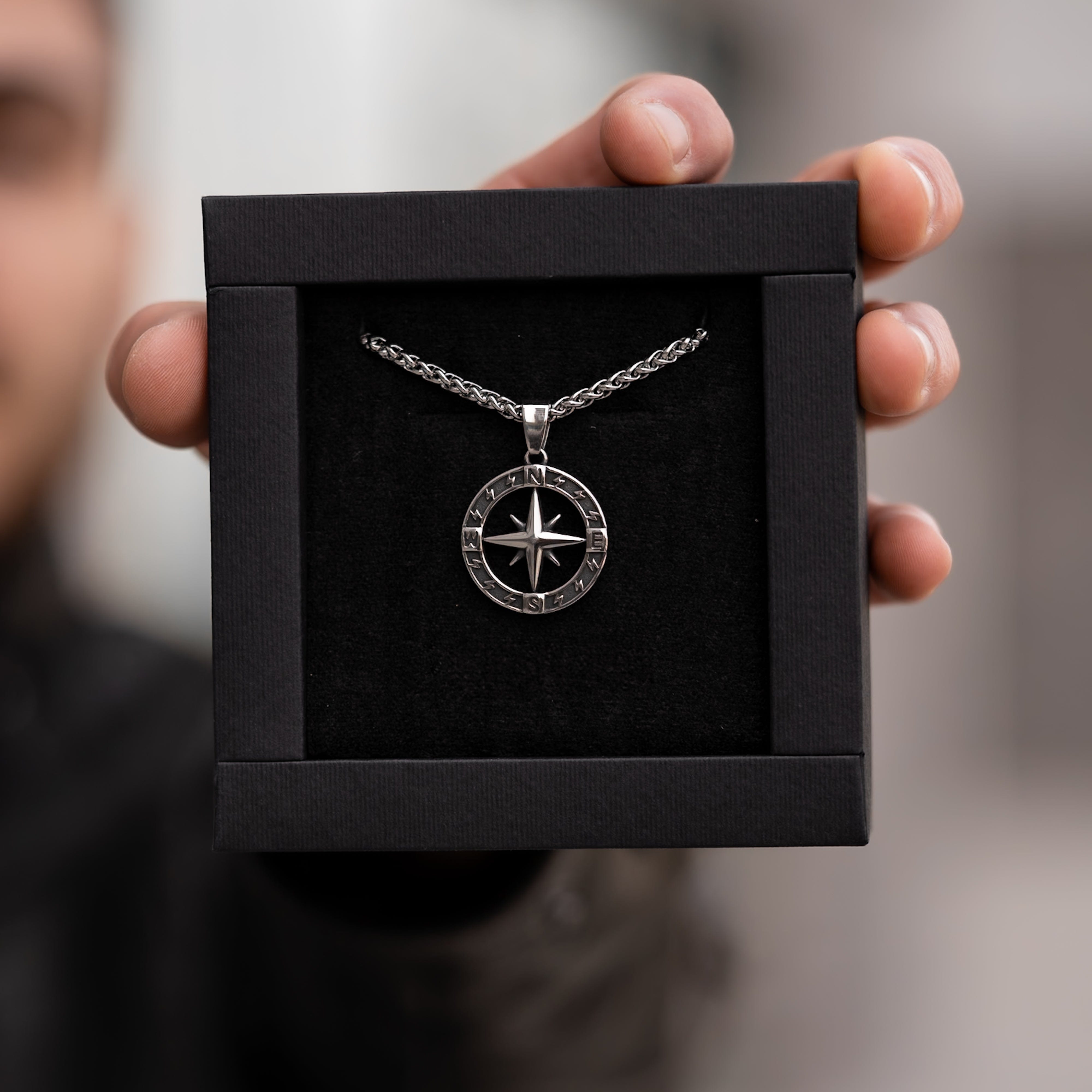 Muskarac drzi u ruci kutiju sa muskom ogrlicom Stellar North. Privezak i lanac HIRUSKI CELIK, srebrna boja, Najbolja cena i prodaja u Srbiji, model 27