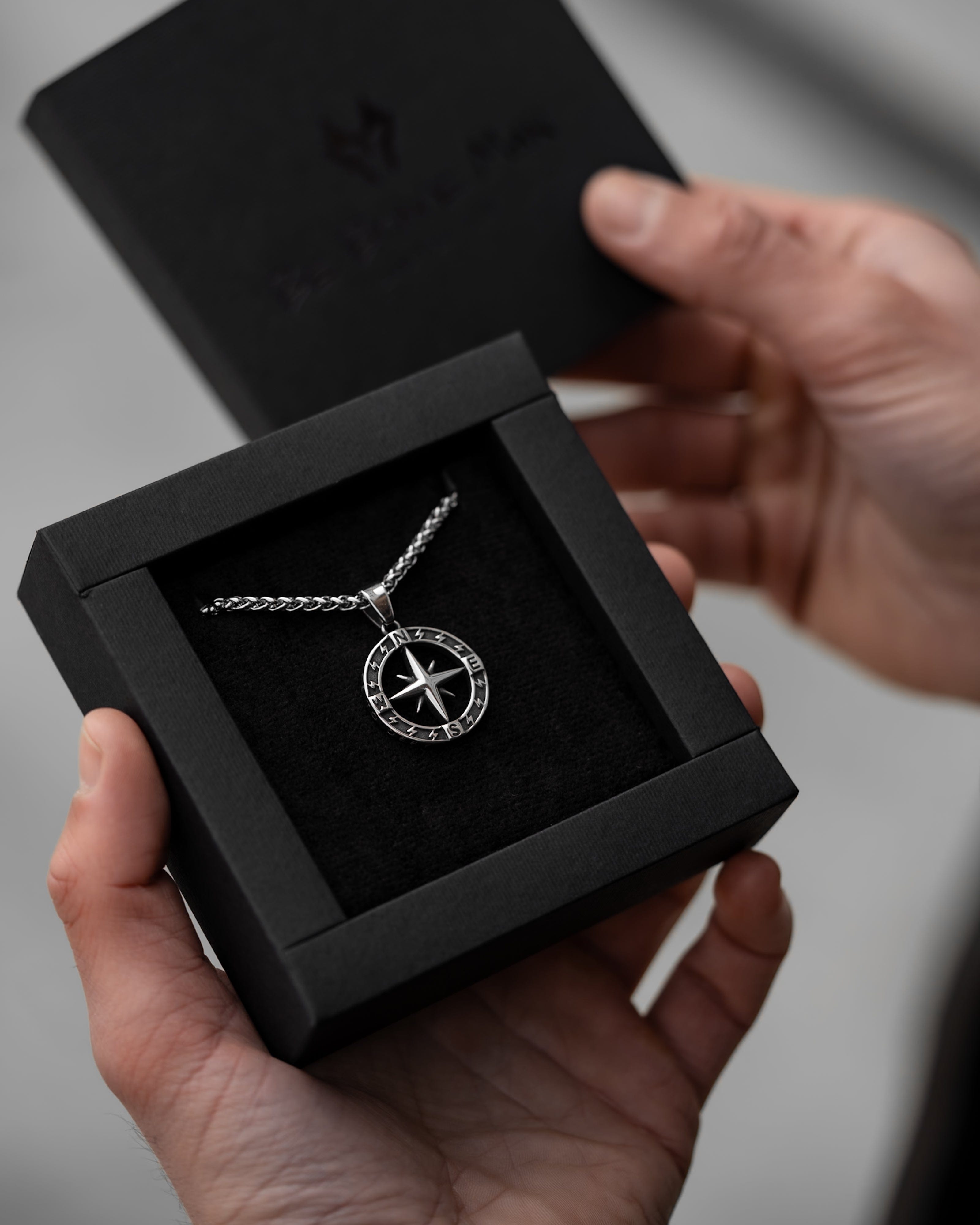 Muskarac drzi kutiju sa muskom ogrlicom Stellar North. Privezak i lanac HIRUSKI CELIK, srebrna boja, model 27